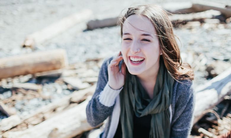 Girl smiling and sitting outside by the water on a sunny day.