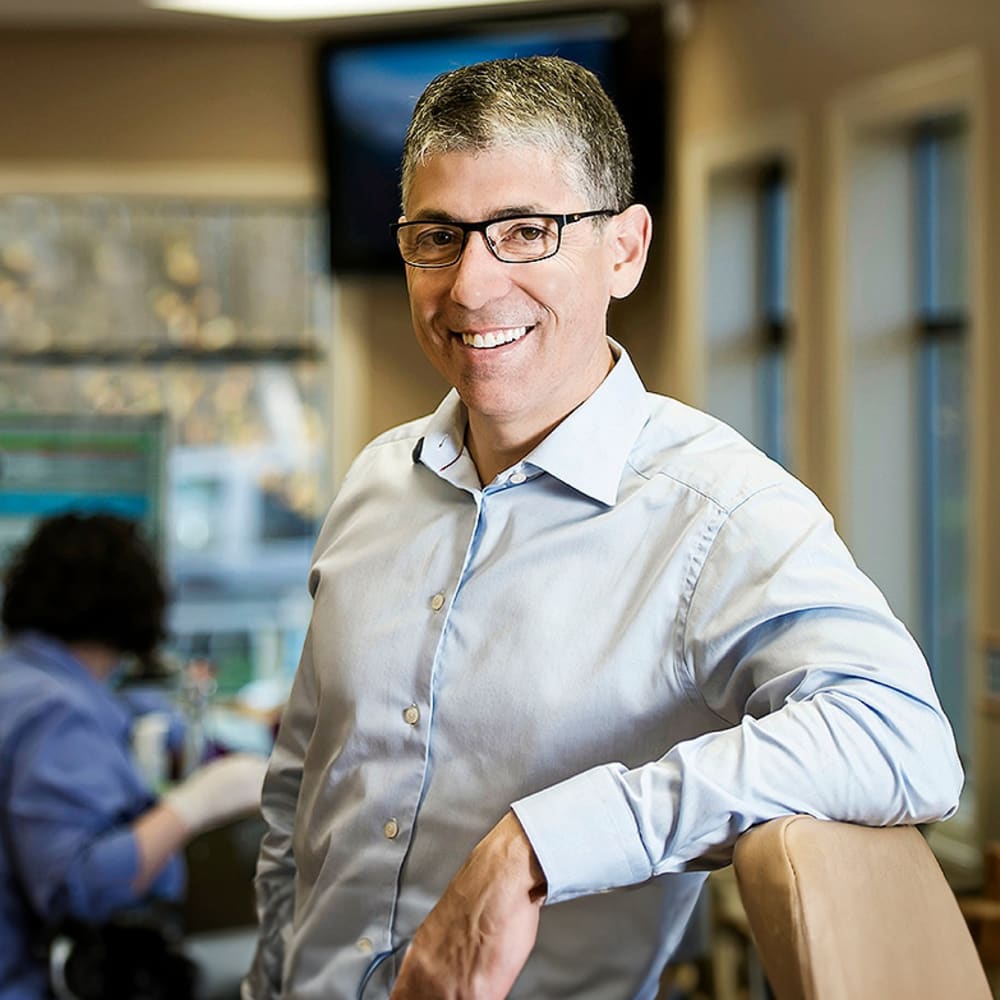 Dr. Helpard smiles and leans on a chair.