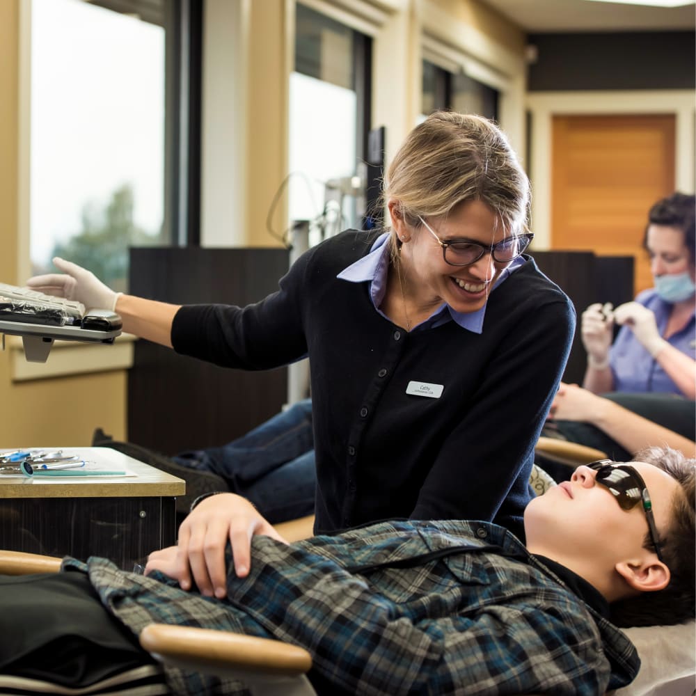 A young boy is laying down in a dental chair and a team member is speaking to him ahead of treatment.