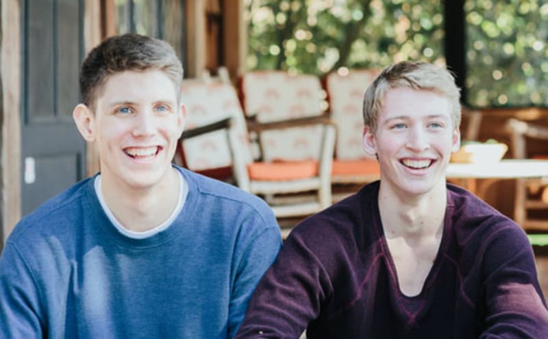 Three teen boys sitting next to eachother in a screened porch while smiling.