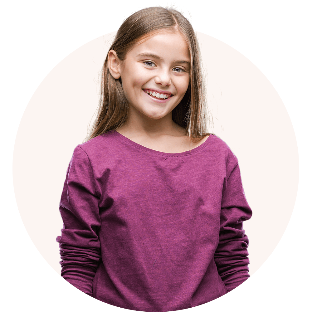 A young girl in a purple shirt, standing and smiling at the camera.