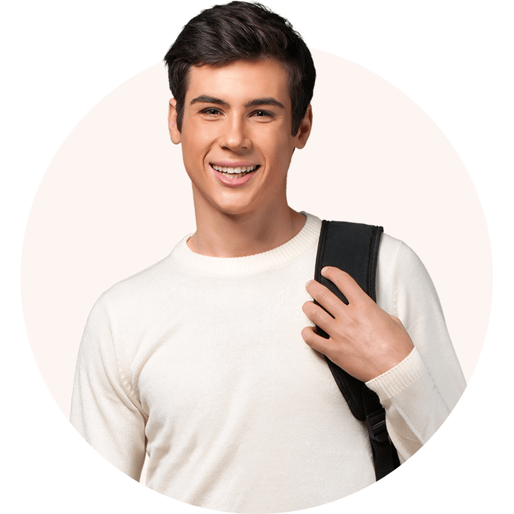 A teenage boy in a white shirt stands smiling at the camera. He has a backpack slung over one shoulder while holding the strap.