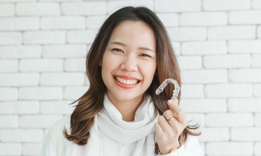 A woman holds up an Invisalign clear aligner.