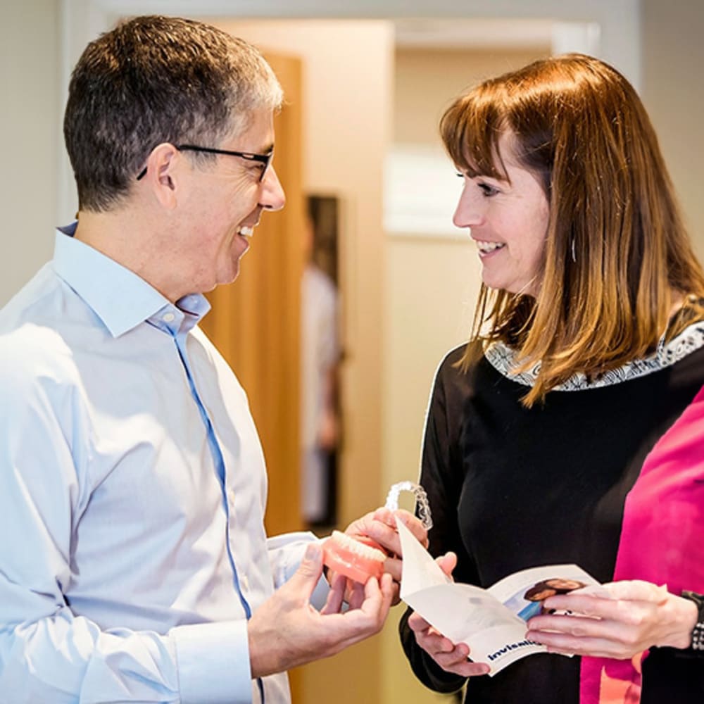 Dr. Helpard shows a female patient about Invisalign. She is holding a brochure and he is holding an aligner tray.