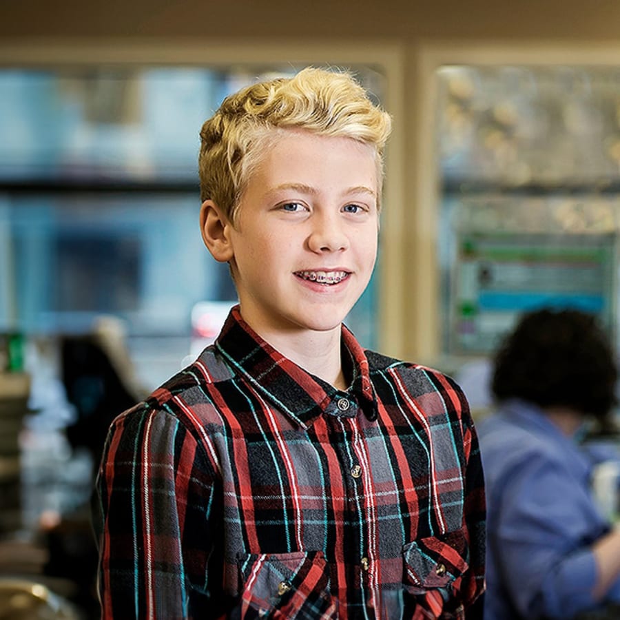 A young patient with blonde hair and blue eyes smiles, showing off braces.